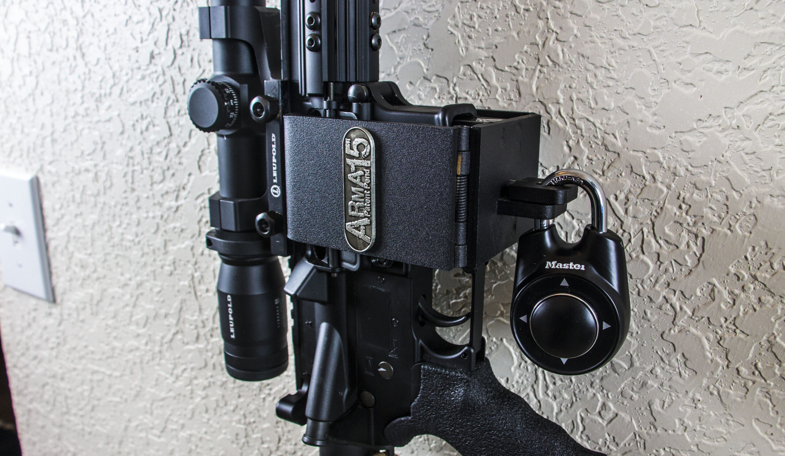 ARmA15 mount securing a vertical AR15 rifle to a wall with a padlock.